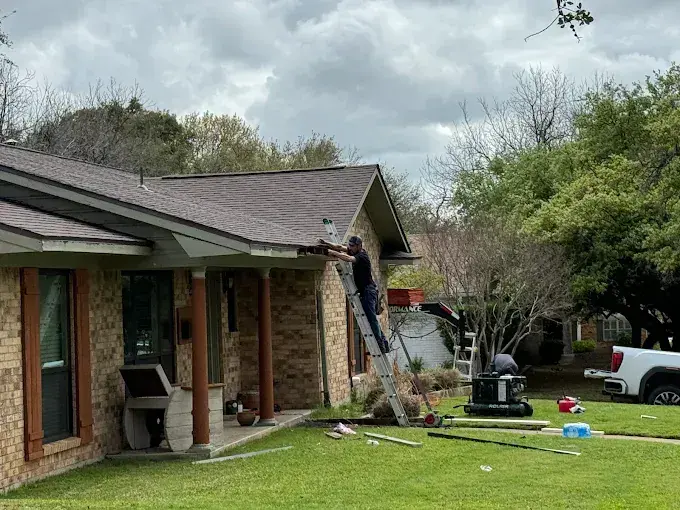 Worker on a ladder fixing the gutter of a brick ranch house, tools on the ground