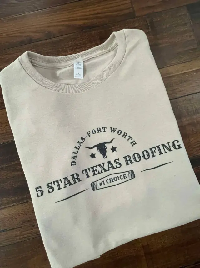 Beige t-shirt with "5 STAR TEXAS ROOFING" logo, including a longhorn, on a wooden surface.