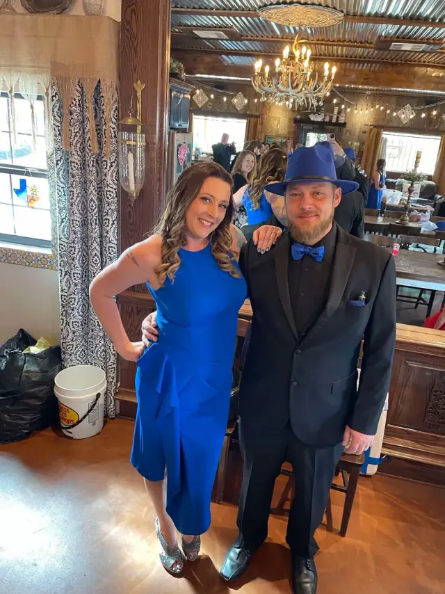 Woman in blue dress and man in suit, posing indoors.