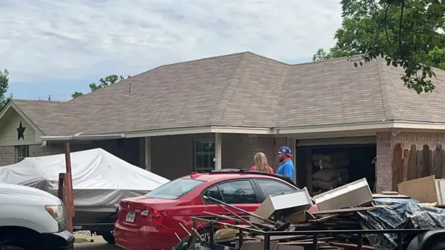 A house with a brown roof and a boat covered in a white tarp. A red car is parked near the house.