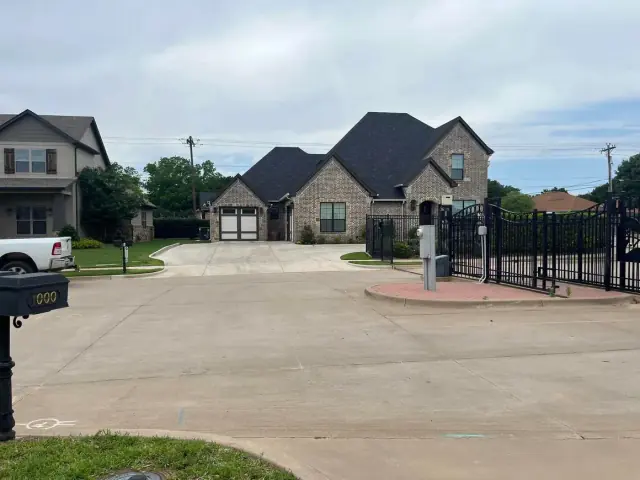 Residential street with brick houses, driveways, and black wrought iron gate.