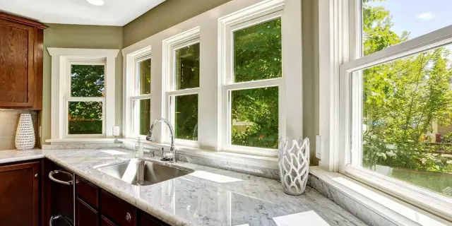 Kitchen interior with countertop, sink, and multiple windows overlooking greenery.