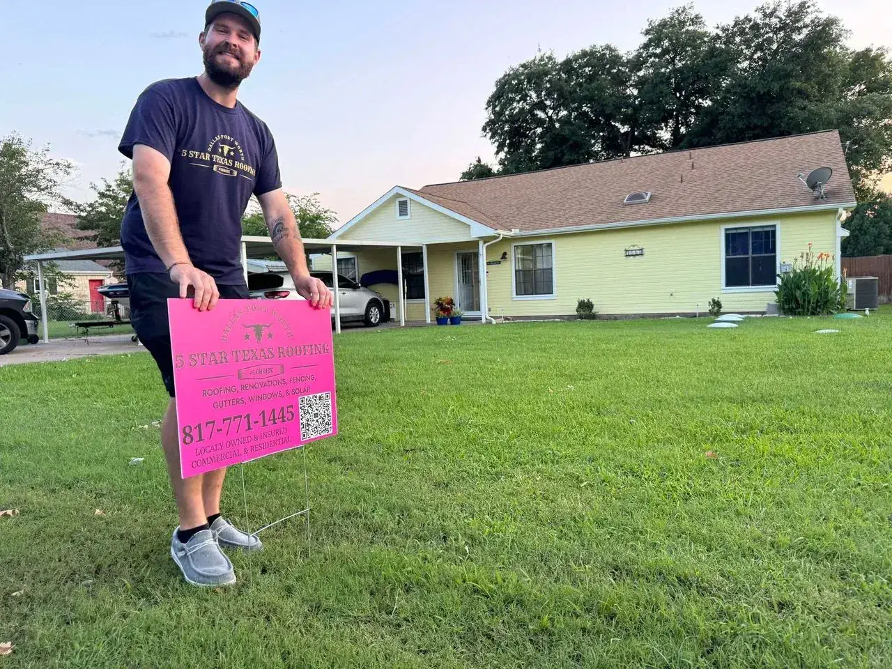 Man holding a pink sign in front of a yellow house. Sign has text and a QR code.