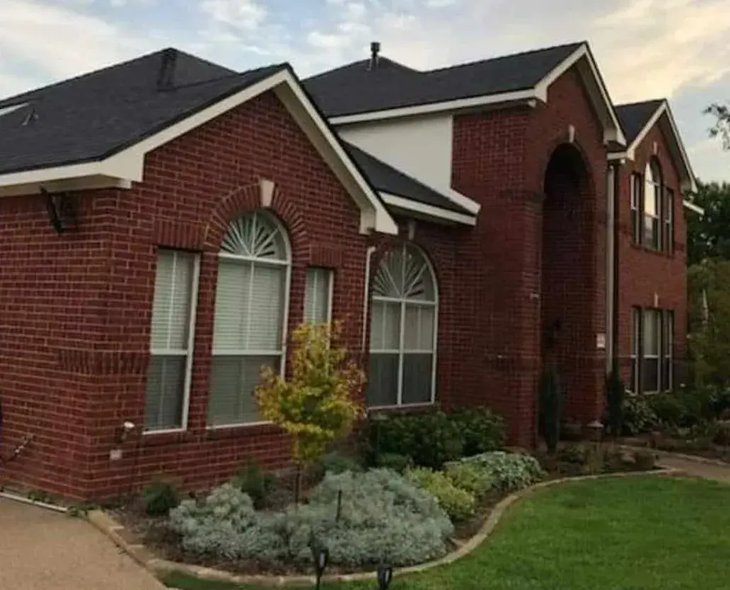 Red brick two-story house with dark roof and arched windows; manicured lawn and landscaping in front.