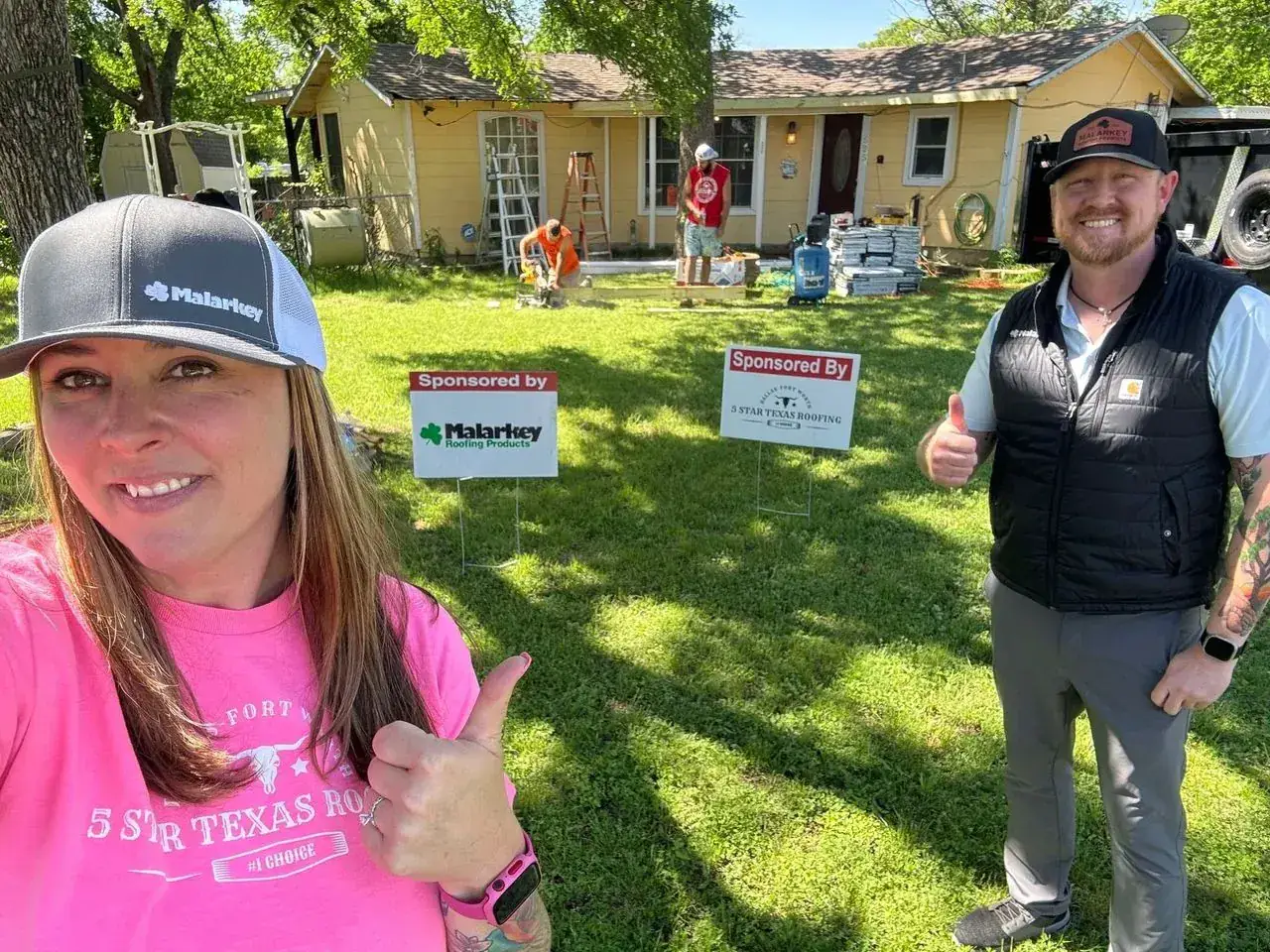 Team member giving a thumbs up beside a sponsored roof replacement at a yellow house