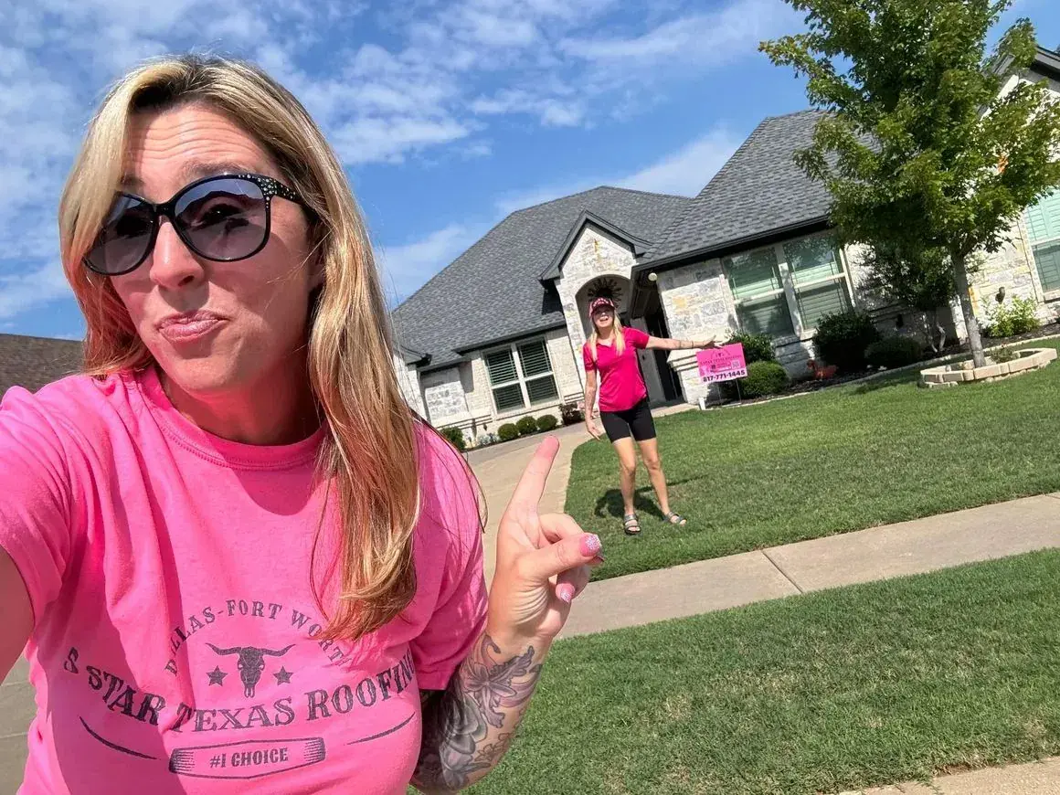 Woman in a pink shirt points something out to a homeowner in front of a house